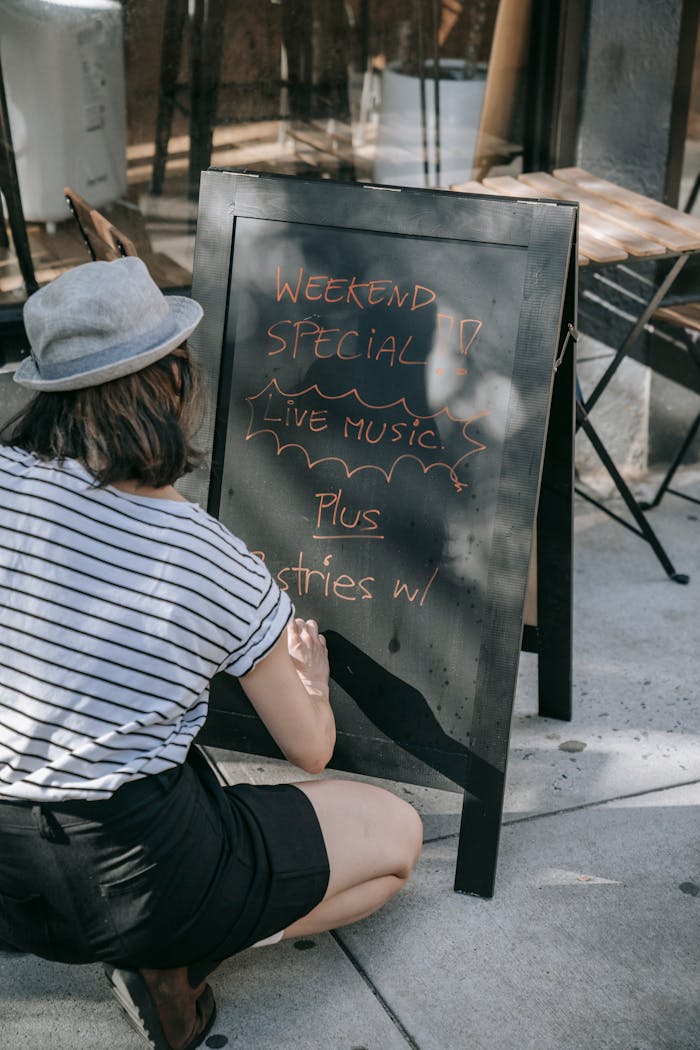 Back view of woman writing live music special on outdoor café chalkboard.