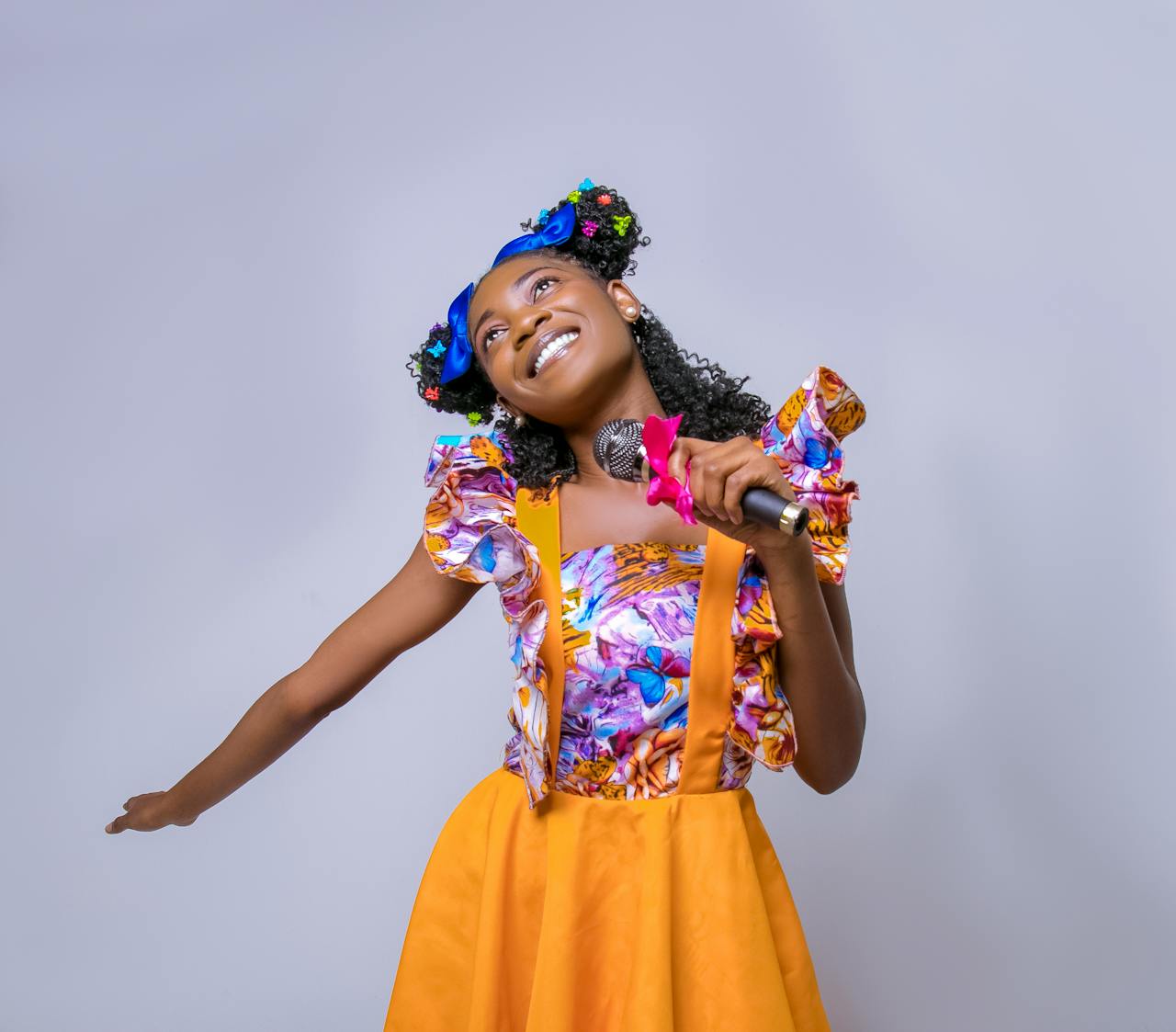 A vibrant woman in colorful attire joyfully singing into a microphone.